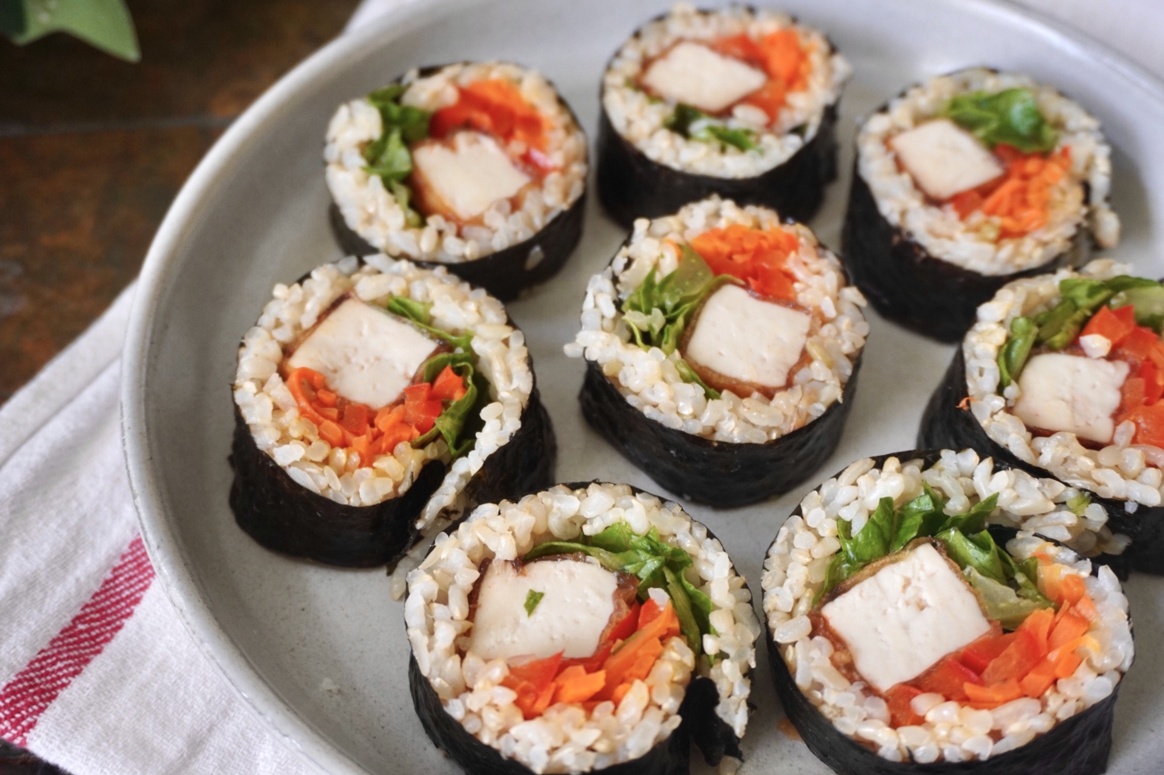 Sliced vegan tofu kimbap rolls on a gray plate, filled with crispy gochujang tofu, carrots, red bell pepper, romaine lettuce, and brown rice wrapped in nori